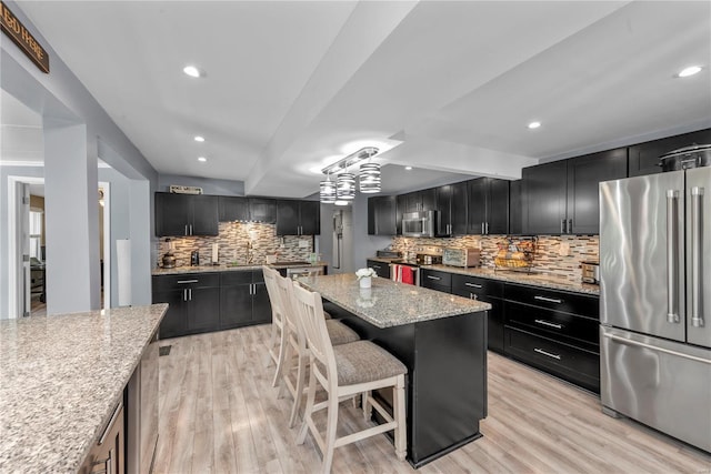 kitchen with stainless steel appliances, light stone counters, dark cabinets, and light wood finished floors