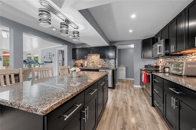 kitchen featuring stainless steel appliances, backsplash, light wood-style floors, dark cabinetry, and baseboards