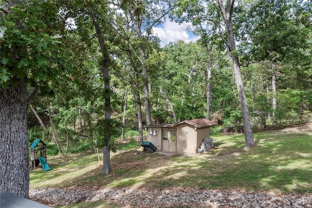 view of yard with a forest view, an outbuilding, a playground, and a storage shed