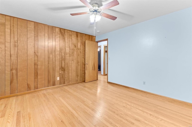 empty room with ceiling fan, light hardwood / wood-style flooring, and wood walls