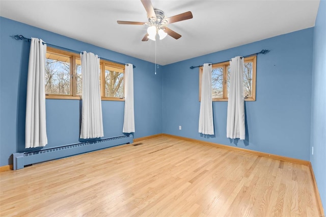 empty room with ceiling fan, a healthy amount of sunlight, baseboard heating, and light hardwood / wood-style floors