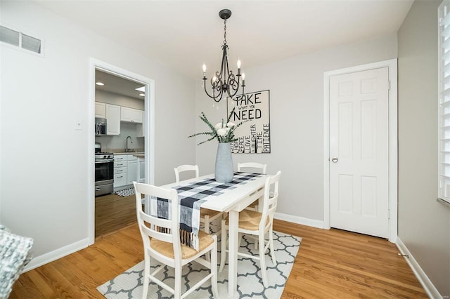 dining space with visible vents, light wood-style floors, baseboards, and a chandelier