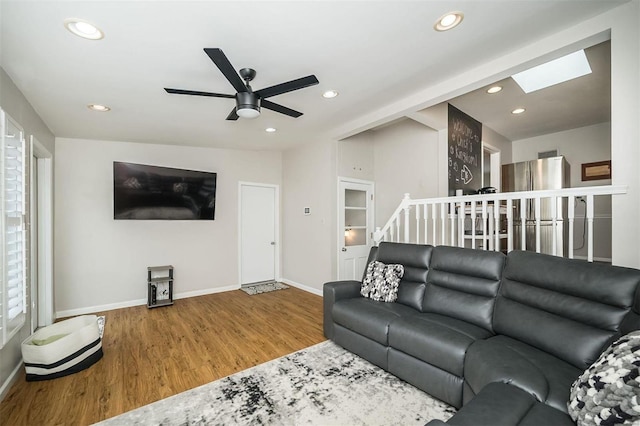 living area with a ceiling fan, wood finished floors, recessed lighting, a skylight, and baseboards