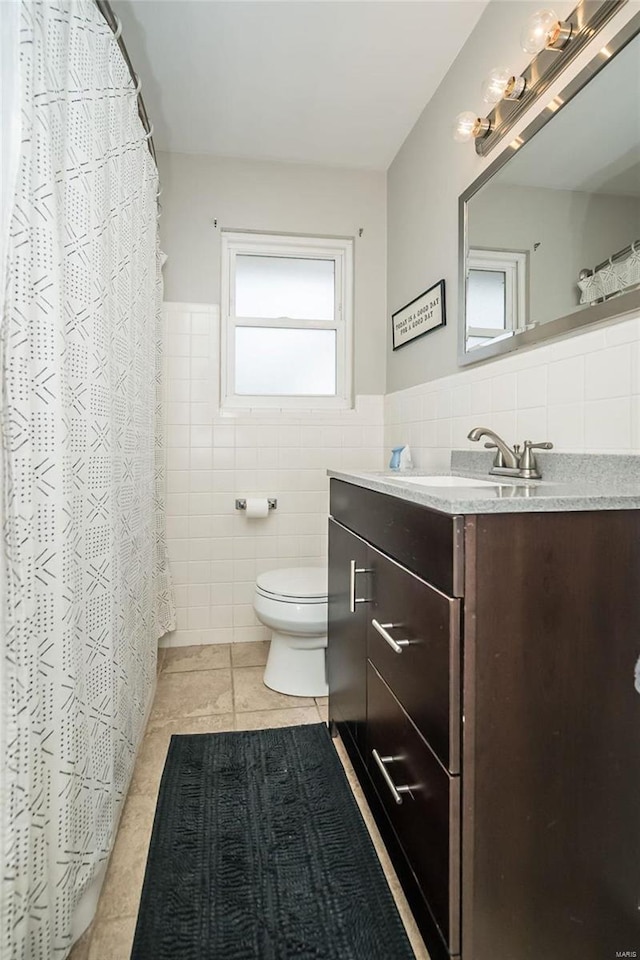 bathroom featuring toilet, vanity, wainscoting, tile patterned floors, and tile walls