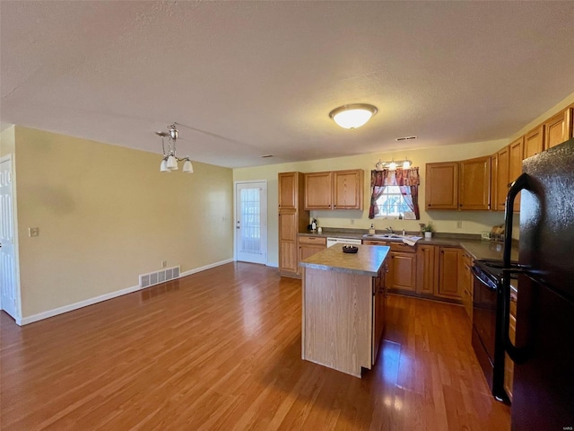 kitchen with pendant lighting, sink, dark hardwood / wood-style flooring, a center island, and black appliances