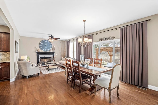 dining room with wood-type flooring, ceiling fan with notable chandelier, and a high end fireplace