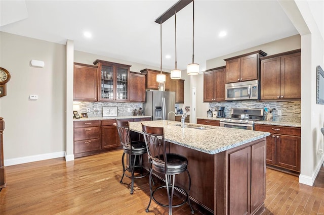 kitchen with sink, light stone counters, decorative light fixtures, a center island with sink, and stainless steel appliances