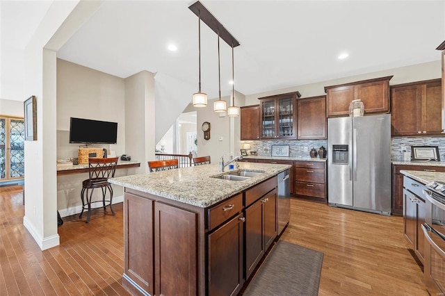 kitchen with a sink, backsplash, wood finished floors, stainless steel appliances, and glass insert cabinets