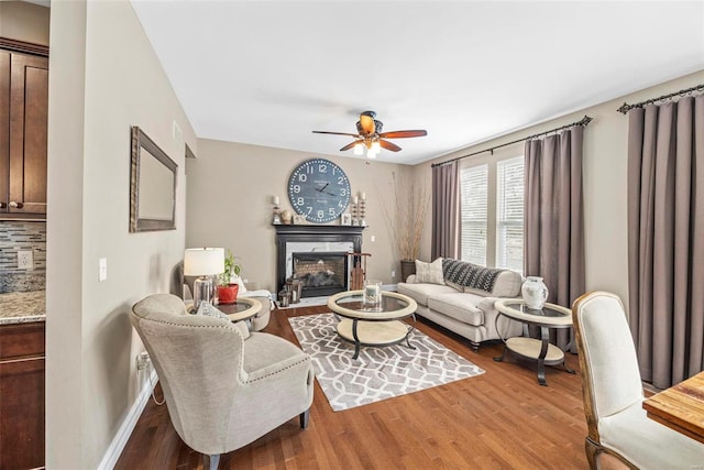 living room with a fireplace, wood finished floors, baseboards, and ceiling fan