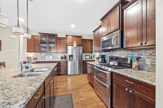 kitchen with light stone countertops, decorative backsplash, appliances with stainless steel finishes, light wood-style floors, and a sink