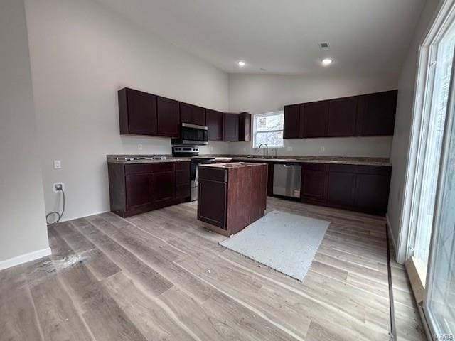 kitchen featuring vaulted ceiling, a kitchen island, dark brown cabinetry, stainless steel appliances, and light hardwood / wood-style flooring