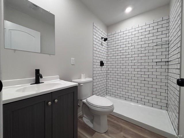 bathroom featuring vanity, toilet, wood-type flooring, and a tile shower