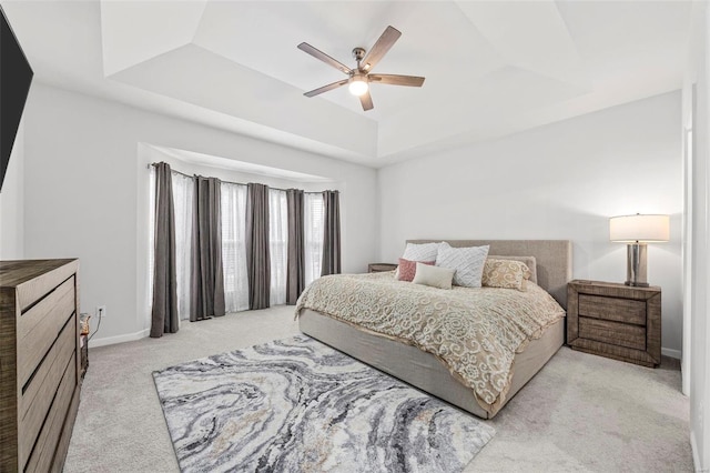 bedroom with a tray ceiling, light colored carpet, and ceiling fan