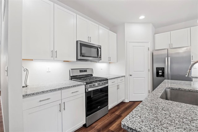 kitchen with dark hardwood / wood-style flooring, light stone countertops, white cabinets, and appliances with stainless steel finishes