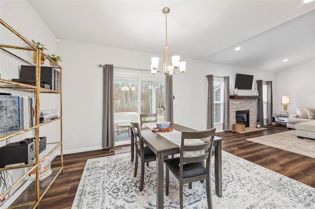 dining room with a stone fireplace, dark wood-type flooring, and an inviting chandelier