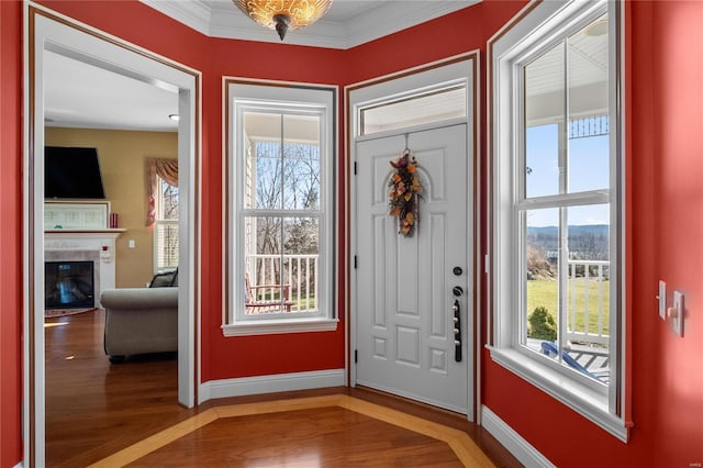 foyer entrance with ornamental molding, light wood-type flooring, a fireplace, and baseboards