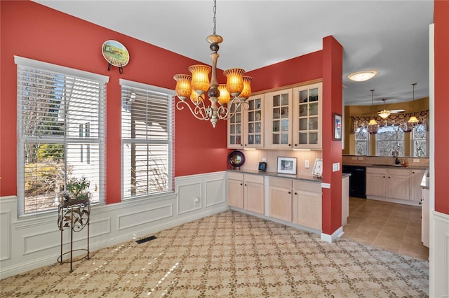 kitchen featuring decorative light fixtures, a wainscoted wall, visible vents, black dishwasher, and glass insert cabinets