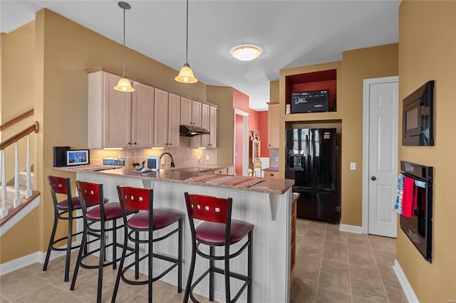 kitchen featuring tasteful backsplash, black appliances, a peninsula, under cabinet range hood, and a kitchen bar