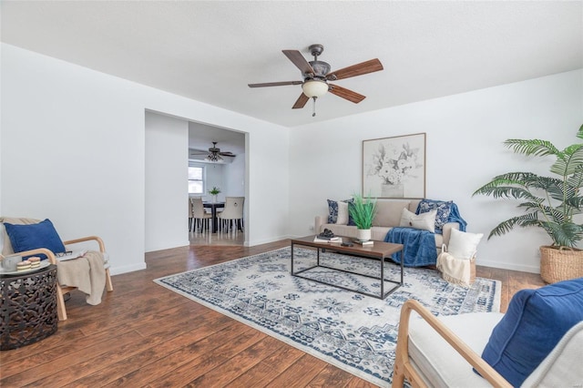 living area featuring dark wood finished floors, baseboards, and ceiling fan