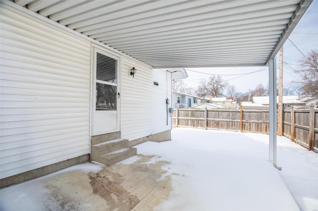 snow covered patio with entry steps, an attached carport, and fence