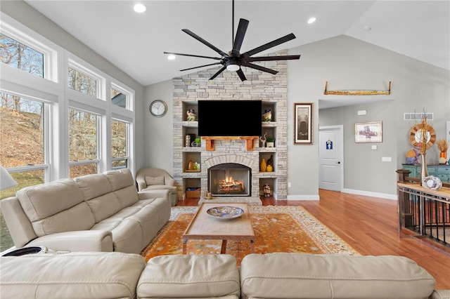 living room with ceiling fan, a stone fireplace, vaulted ceiling, and light wood-type flooring