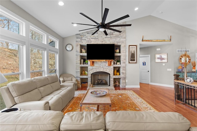 living room with a stone fireplace, light hardwood / wood-style flooring, ceiling fan, and vaulted ceiling