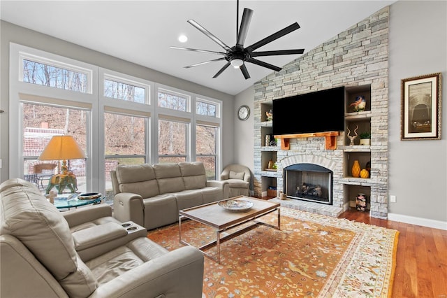 living room featuring high vaulted ceiling, a stone fireplace, light hardwood / wood-style floors, and ceiling fan