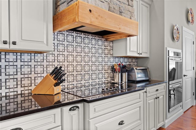 kitchen featuring white cabinetry, premium range hood, black electric stovetop, and backsplash