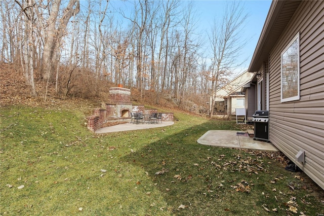 view of yard featuring an outdoor brick fireplace and a patio area