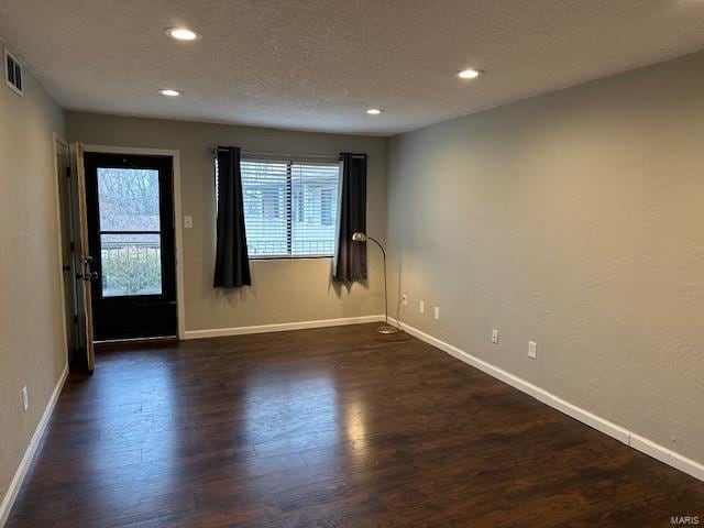 empty room with a textured ceiling, baseboards, dark wood-style flooring, and recessed lighting