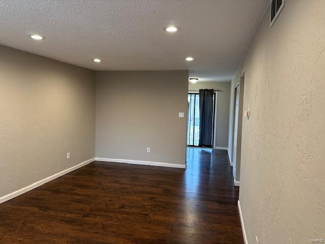 spare room with dark wood-style flooring, visible vents, a textured wall, a textured ceiling, and baseboards