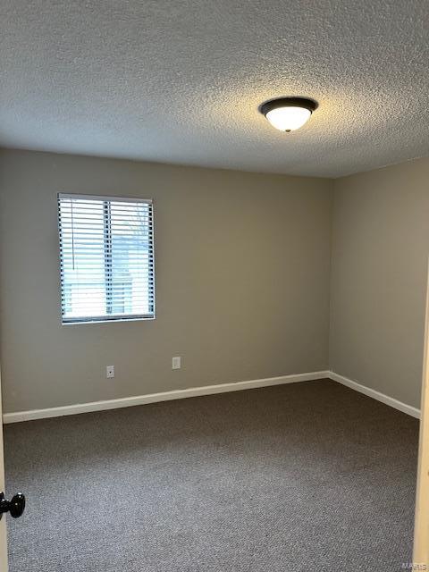 unfurnished room with a textured ceiling, dark colored carpet, and baseboards