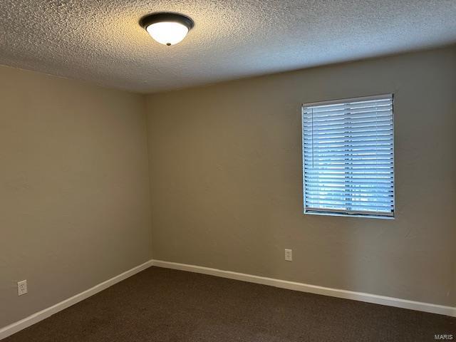 spare room featuring dark colored carpet and baseboards