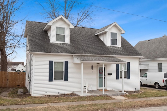 cape cod home featuring a porch, a shingled roof, and fence