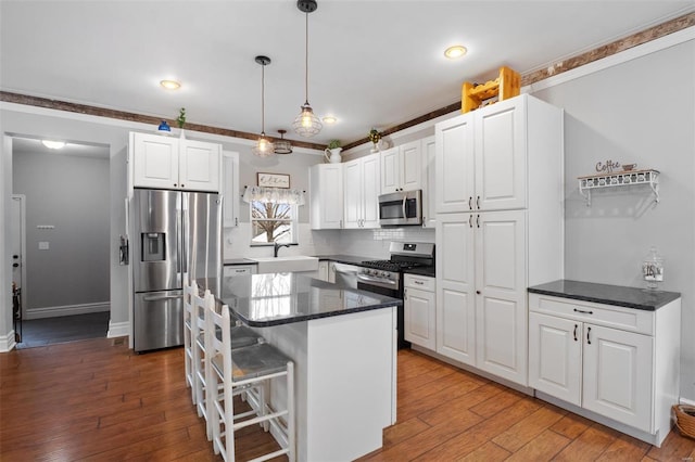 kitchen featuring hardwood / wood-style flooring, a sink, white cabinets, appliances with stainless steel finishes, and decorative light fixtures