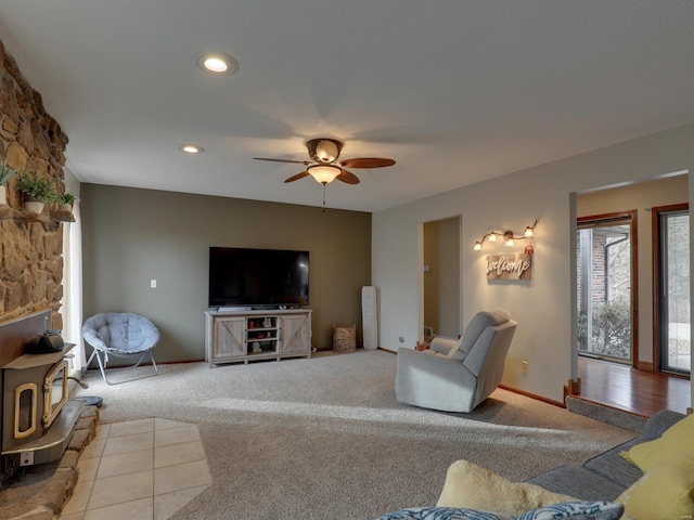 living room with a wood stove, light colored carpet, and ceiling fan