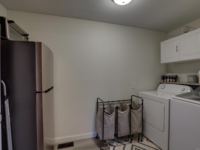 washroom with independent washer and dryer, cabinets, and a textured ceiling