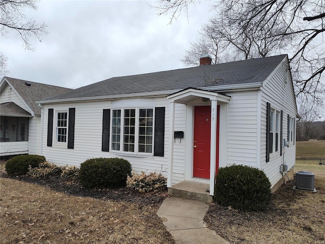 view of front of house featuring cooling unit, roof with shingles, and a chimney