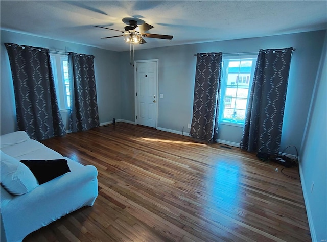 living area with a ceiling fan, a textured ceiling, baseboards, and wood finished floors