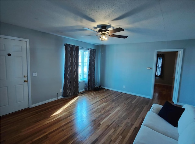 unfurnished living room with ceiling fan, a textured ceiling, baseboards, and wood finished floors