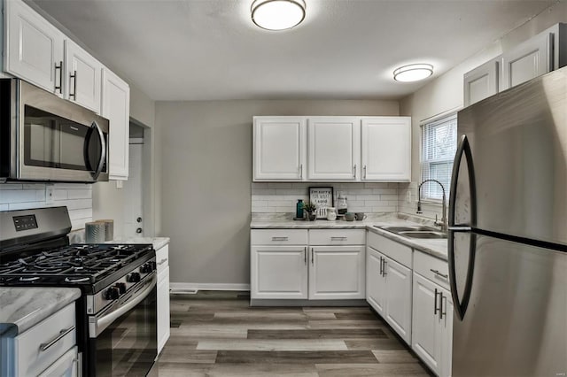 kitchen with appliances with stainless steel finishes, white cabinetry, wood-type flooring, sink, and decorative backsplash