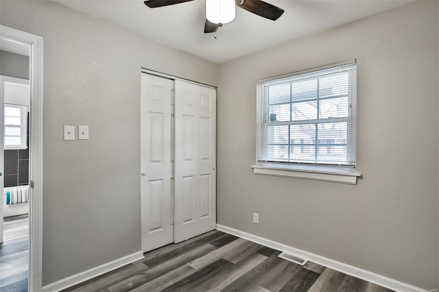 unfurnished bedroom with dark wood-type flooring, a closet, ceiling fan, and multiple windows