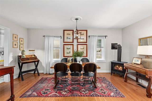 dining area with a notable chandelier, a wood stove, and light wood-type flooring