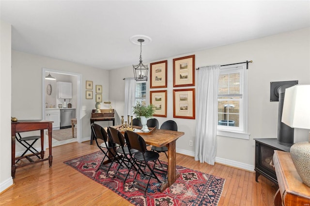 dining area featuring light hardwood / wood-style flooring, plenty of natural light, an inviting chandelier, and a wood stove