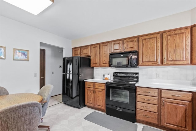 kitchen featuring brown cabinets, light countertops, black appliances, and tasteful backsplash