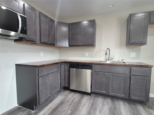 kitchen featuring appliances with stainless steel finishes, sink, wood-type flooring, and butcher block countertops