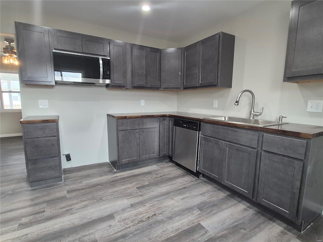 kitchen with appliances with stainless steel finishes, sink, wood counters, and light hardwood / wood-style flooring