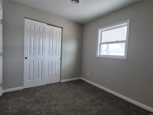 unfurnished bedroom with dark carpet and a closet