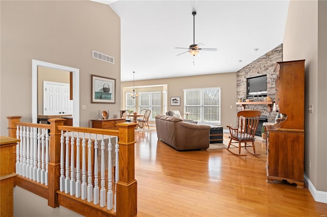 living room with high vaulted ceiling, ceiling fan with notable chandelier, a fireplace, and light hardwood / wood-style flooring