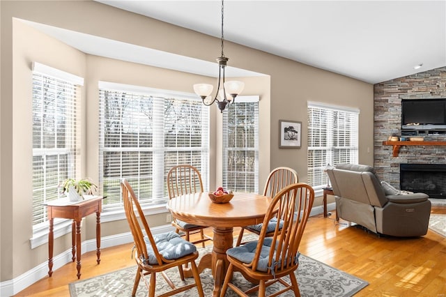 dining space featuring lofted ceiling, light wood-type flooring, a chandelier, and a fireplace